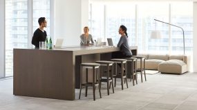 Three people standing/sitting at low community/conference table with bar stool style chairs in office